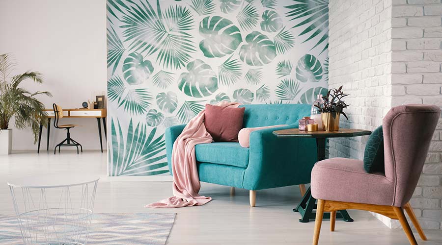Decoração com papel de parede: a imagem mostra um sofá em frente a um papel de parede estampado com grande folhas de planta.
