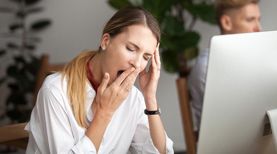 Mulher bocejando em ambiente de trabalho, sinalizando que não teve uma boa noite de sono.