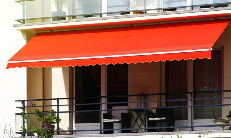 Modelos de cortinas, persianas e toldos: imagem mostra área externa de casa com toldo vermelho, e na parte interna uma cortina ou persiana